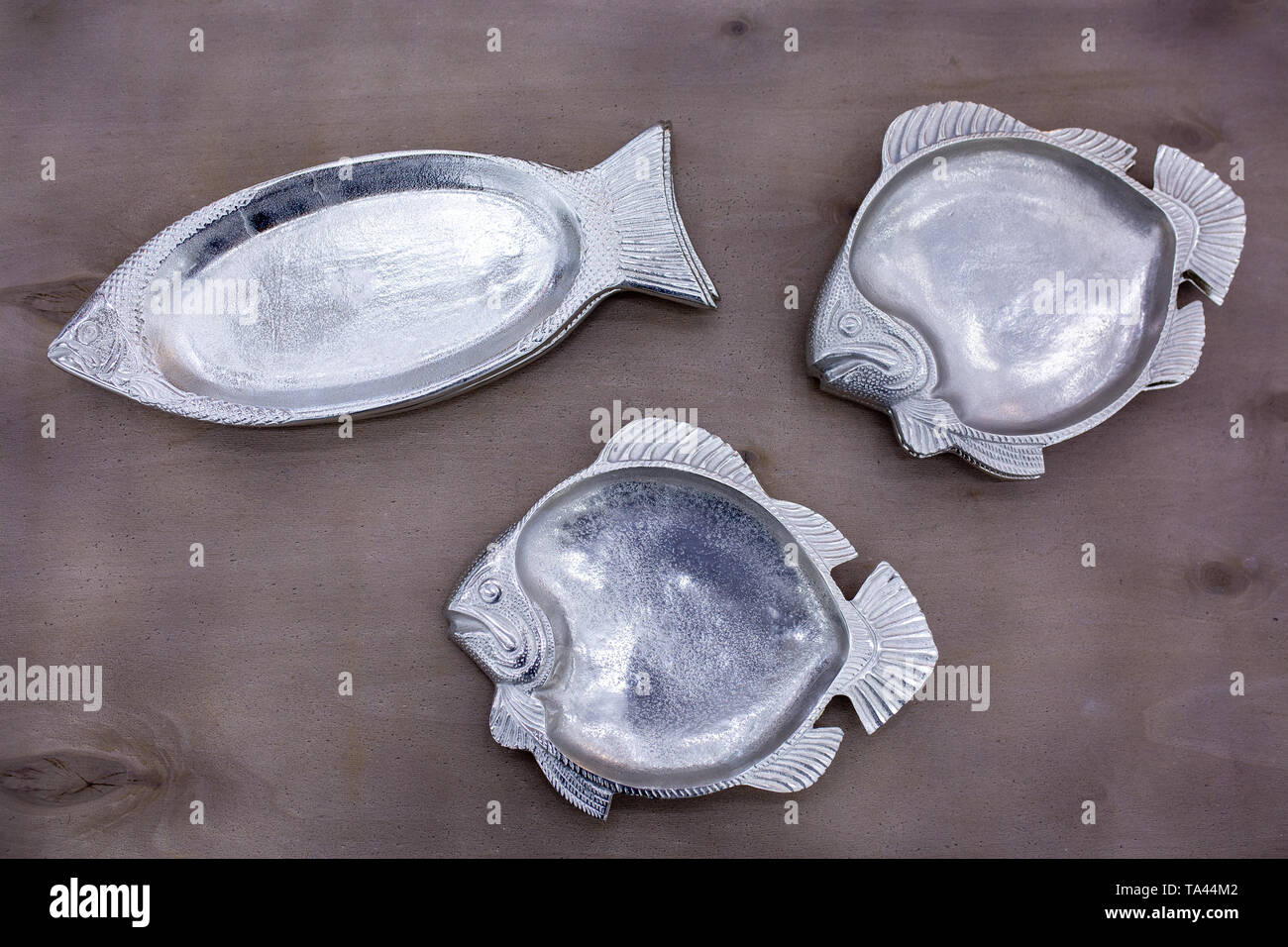 empty fish-shaped silver plates on a wooden table Stock Photo