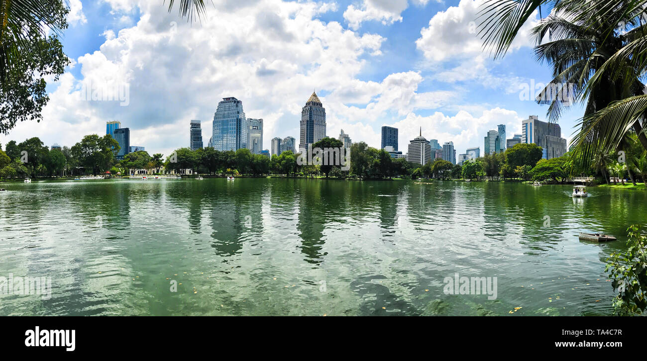 Panorama of Pond with Pedal boat at Lumpini park or Suan Lumpini, Bangkok, Thailand. Office buildings and condominiums with white clouds and blue sky. Stock Photo