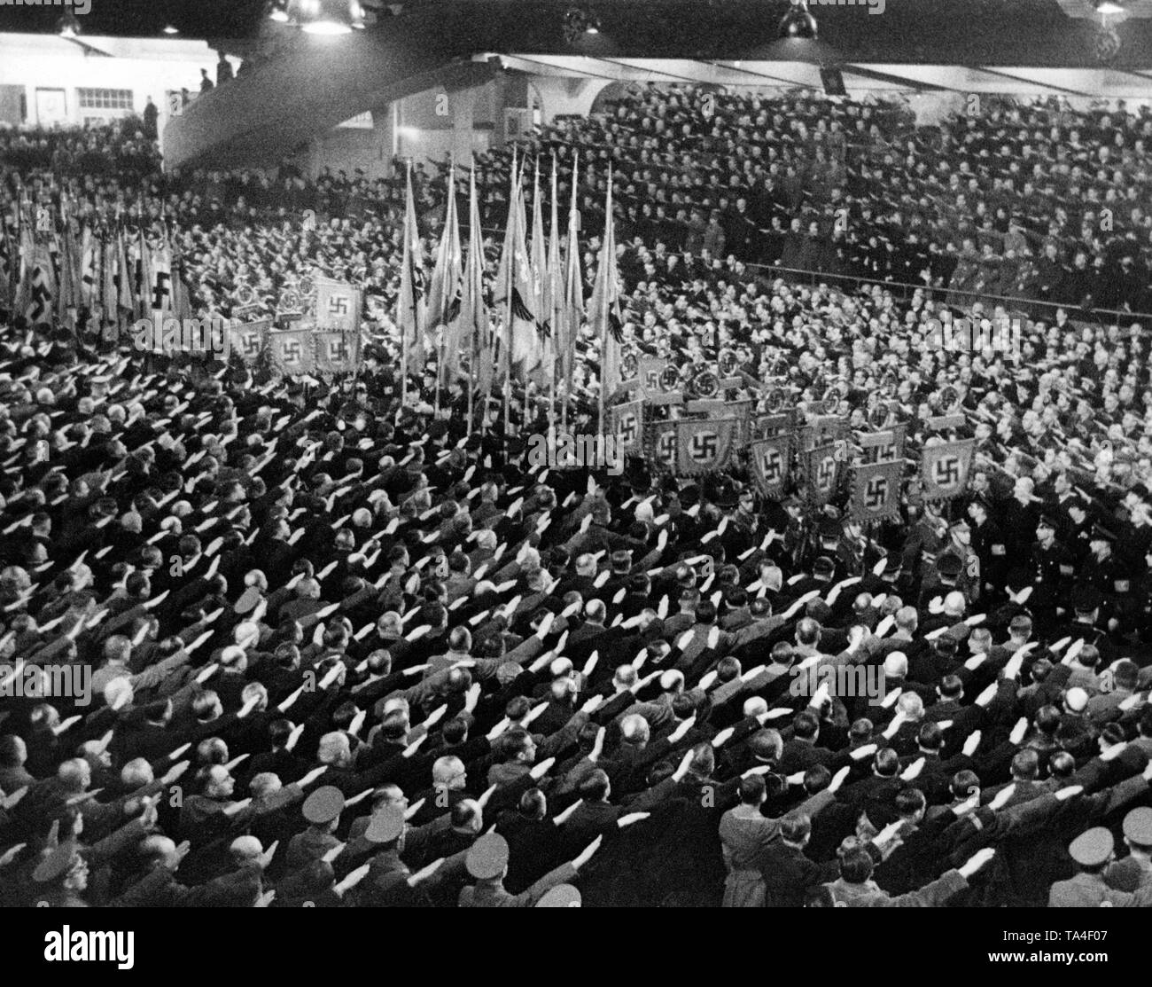 At a rally of the NSDAP, where Adolf Hitler is giving a speech, the participants rise to the entry of the flags of the Nazi regime, and raise their arms to perform the Nazi salute. Photo: Schwahn Stock Photo