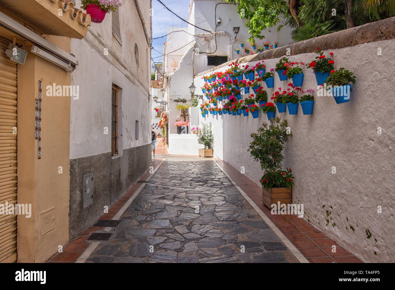 A traditional Spanish street with cobbled road and flowers on the wall in summer Stock Photo