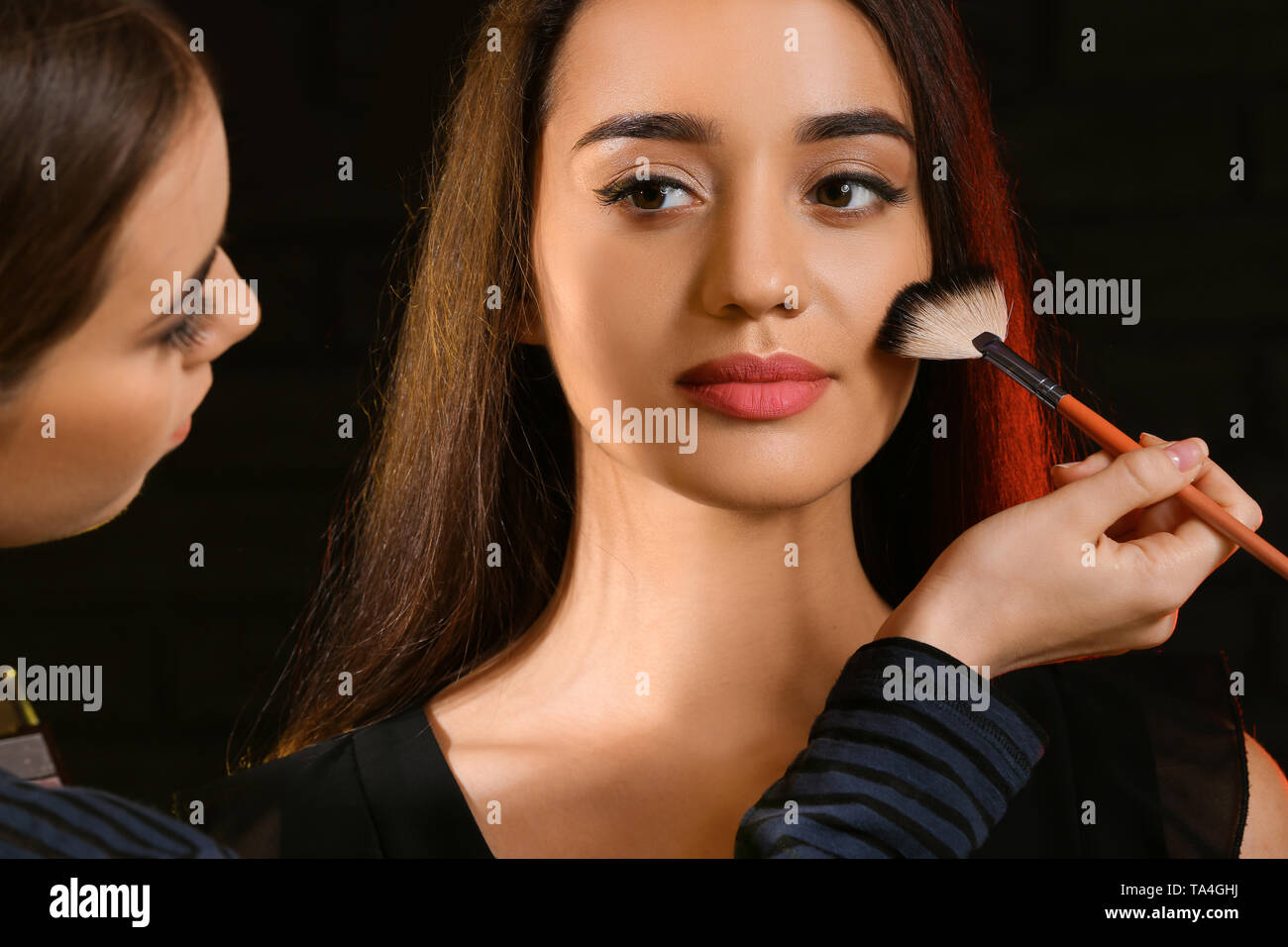 Professional makeup artist working with young model on dark background Stock Photo