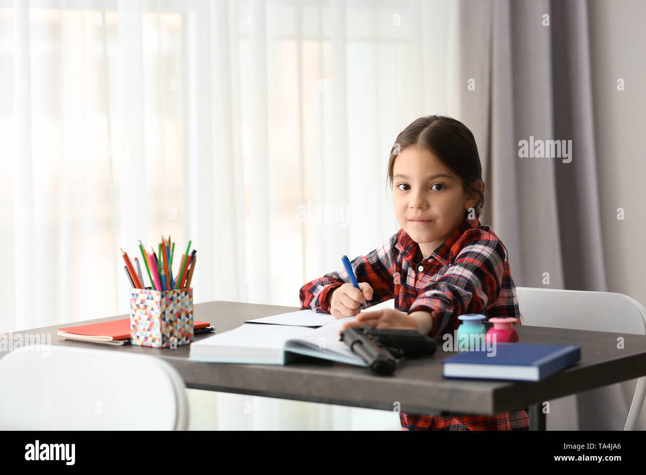 Cute Little Girl With Gun Sitting At Desk In Classroom Concept Of