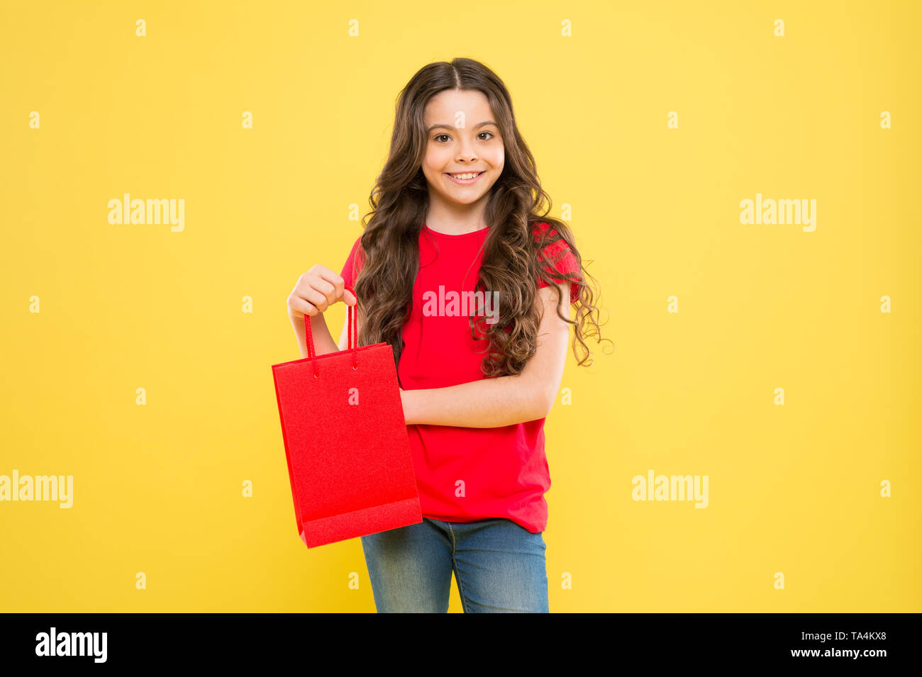 delivery service. child on yellow background. shopping. child with shopping bag. happy girl with long curly hair. little beauty shopaholic. Holiday present. little girl shopping online. happy shopper. Stock Photo