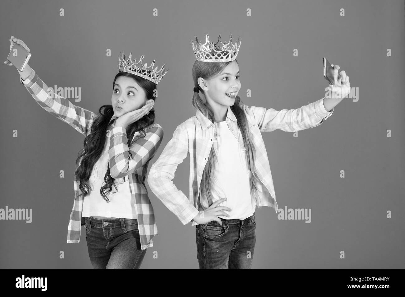 Spoiled children concept. Egocentric princess. Kids wear golden crowns symbol princess. Warning signs of spoiled child. Avoid raising spoiled kids. Girls taking selfie photo smartphone camera. Stock Photo