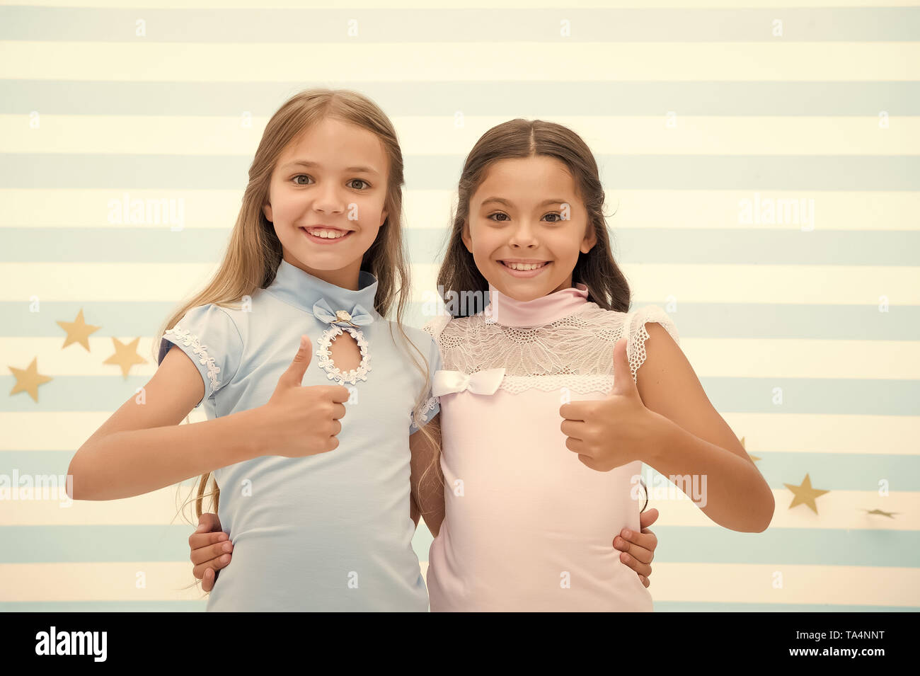 Girls smiling happy faces hug each other and show thumbs up gesture. Girls children best friends hugs. Happy childhood concept. Kids schoolgirls preteens happy together. Friendship from childhood. Stock Photo