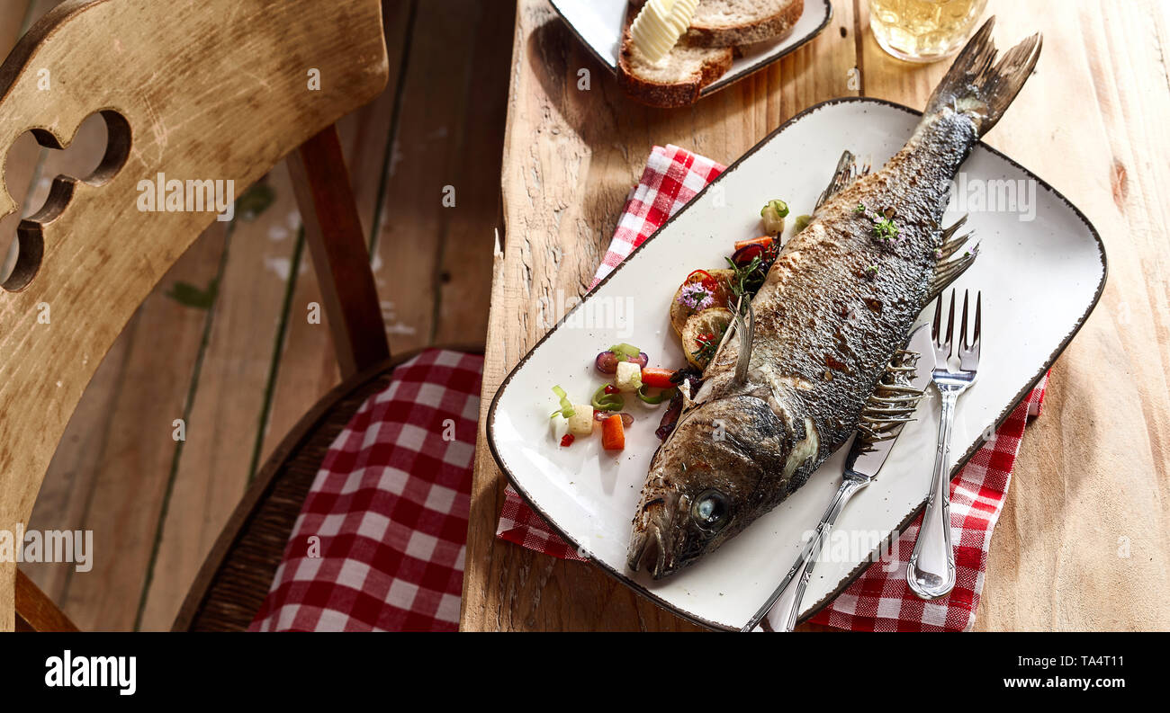 Whole grilled sea bass served on a platter garnished with vegetables on