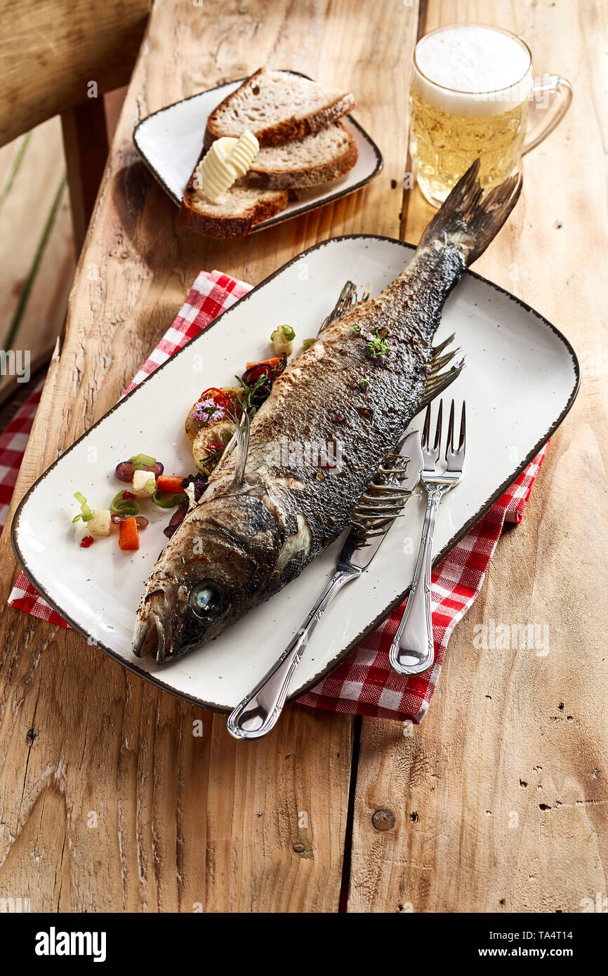 Whole oven roasted sea bass fish on a plate served with slices of rye