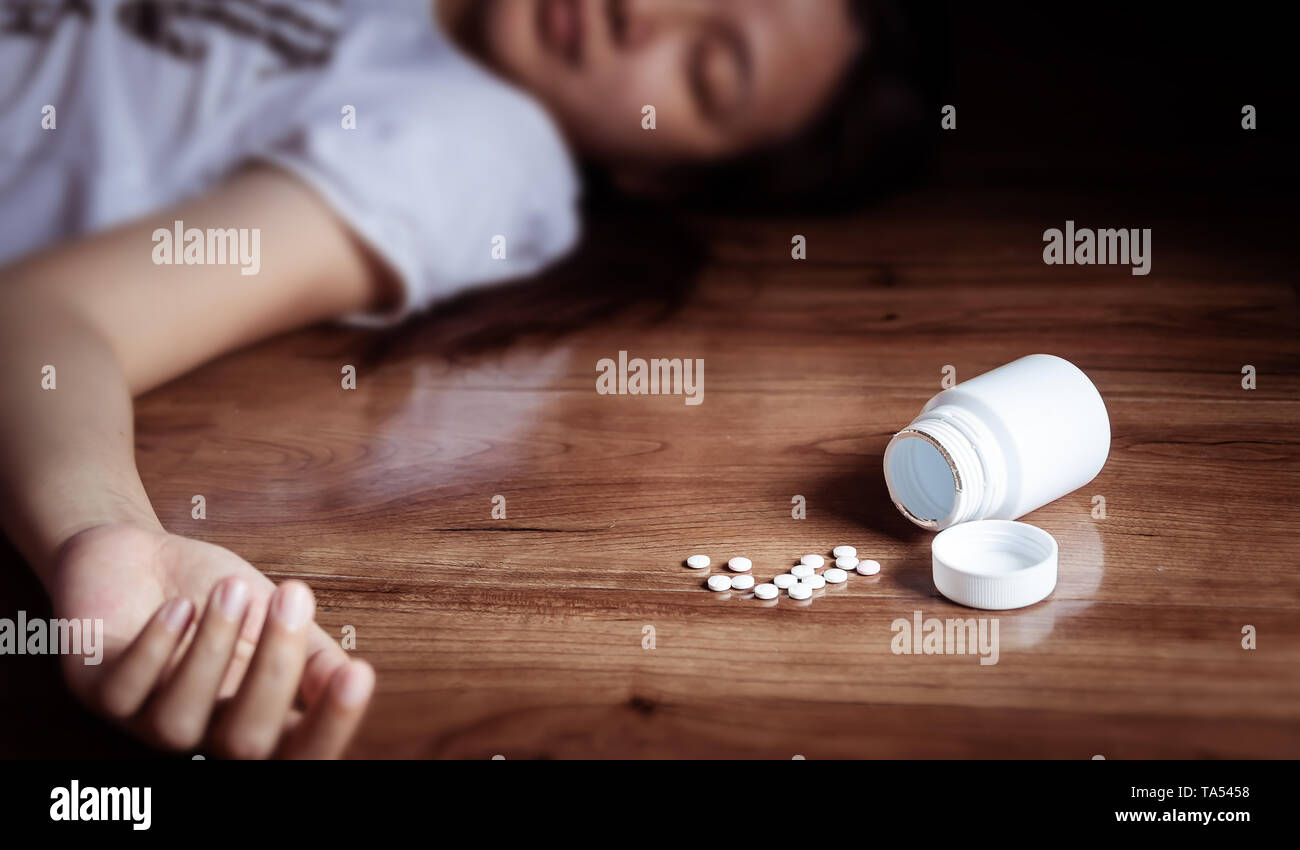 overdose concept. close up of pills and woman taking medicine overdose lying on the floor with open pills bottle Stock Photo