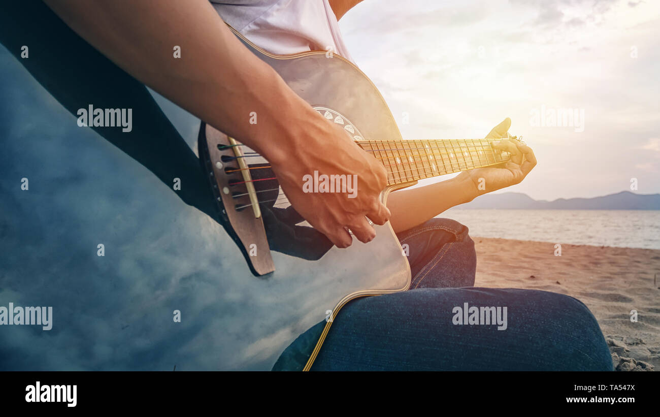 man's hands playing acoustic guitar, capture chords by finger on sandy beach at sunset time. playing music concept Stock Photo