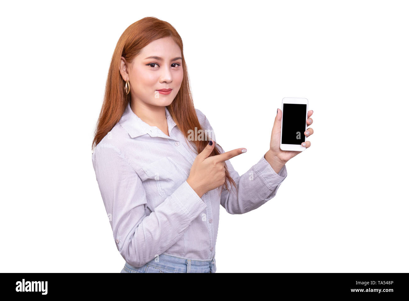 smiling Asian woman standing in casual shirt holding mobile phone and  pointing on smartphone isolated on white background with clipping path Stock Photo