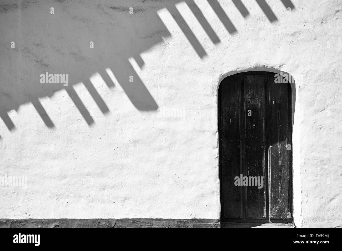 A white wall with roof shadows and a wood door at La Purisima Mission in Lompoc, California. Stock Photo