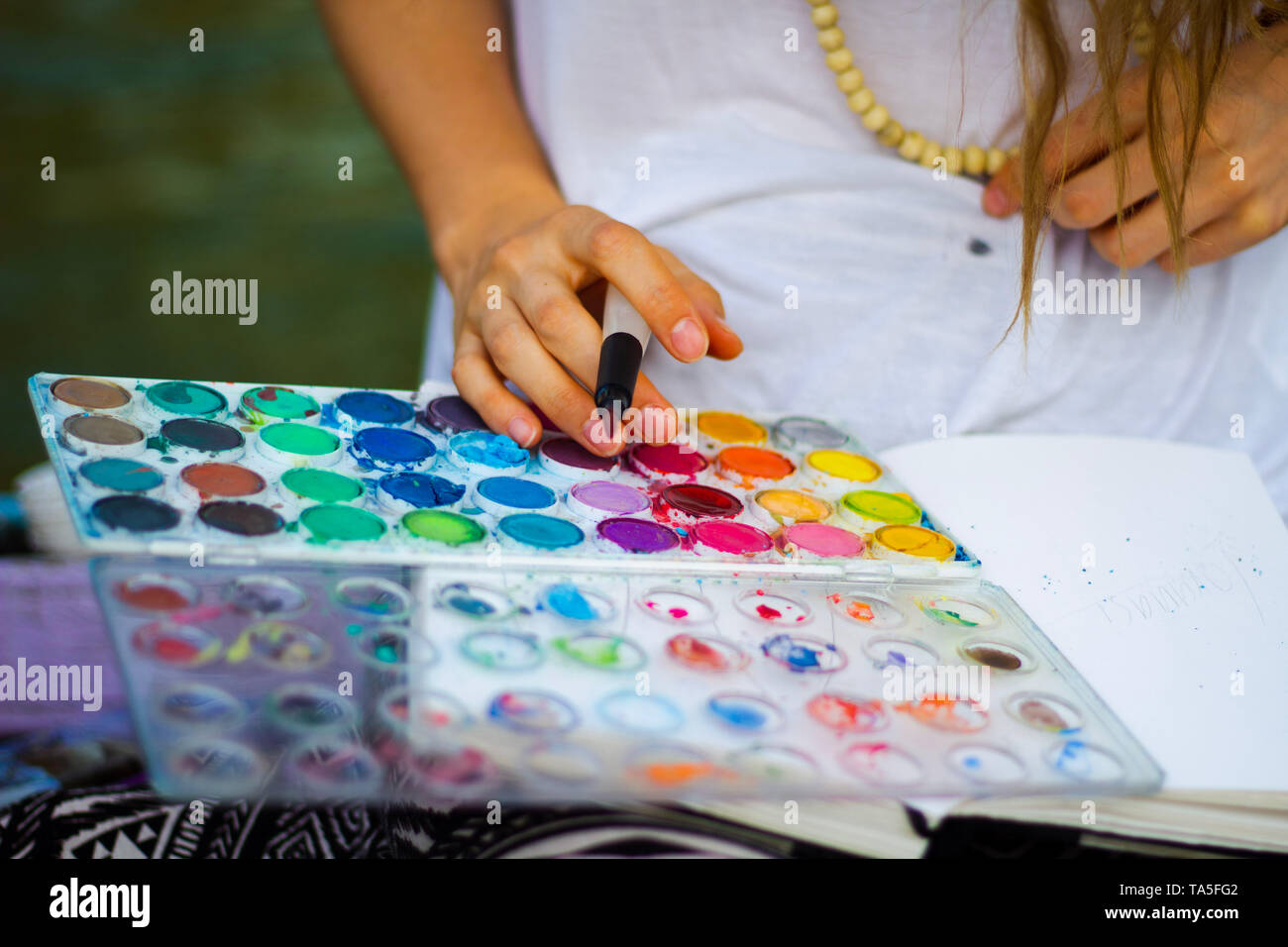 Girl holding water brush pen over color palette choosing color to paint watercolor style illustration. Stock Photo