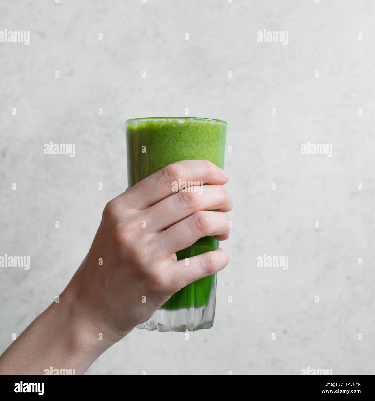 Green smoothie in hand. Female hand holding glass of green spinach detox smoothie, copy space. Stock Photo