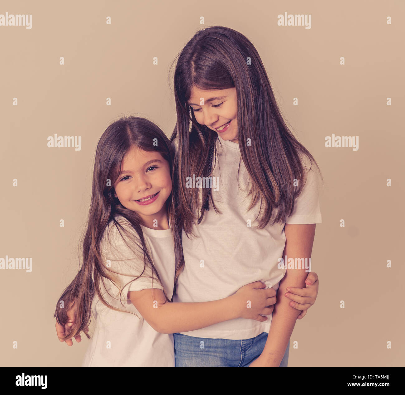 Cute portrait of two cheerful siblings girls sisters having fun together hugging and laughing posing for the camera. Studio shot with copy space. In F Stock Photo