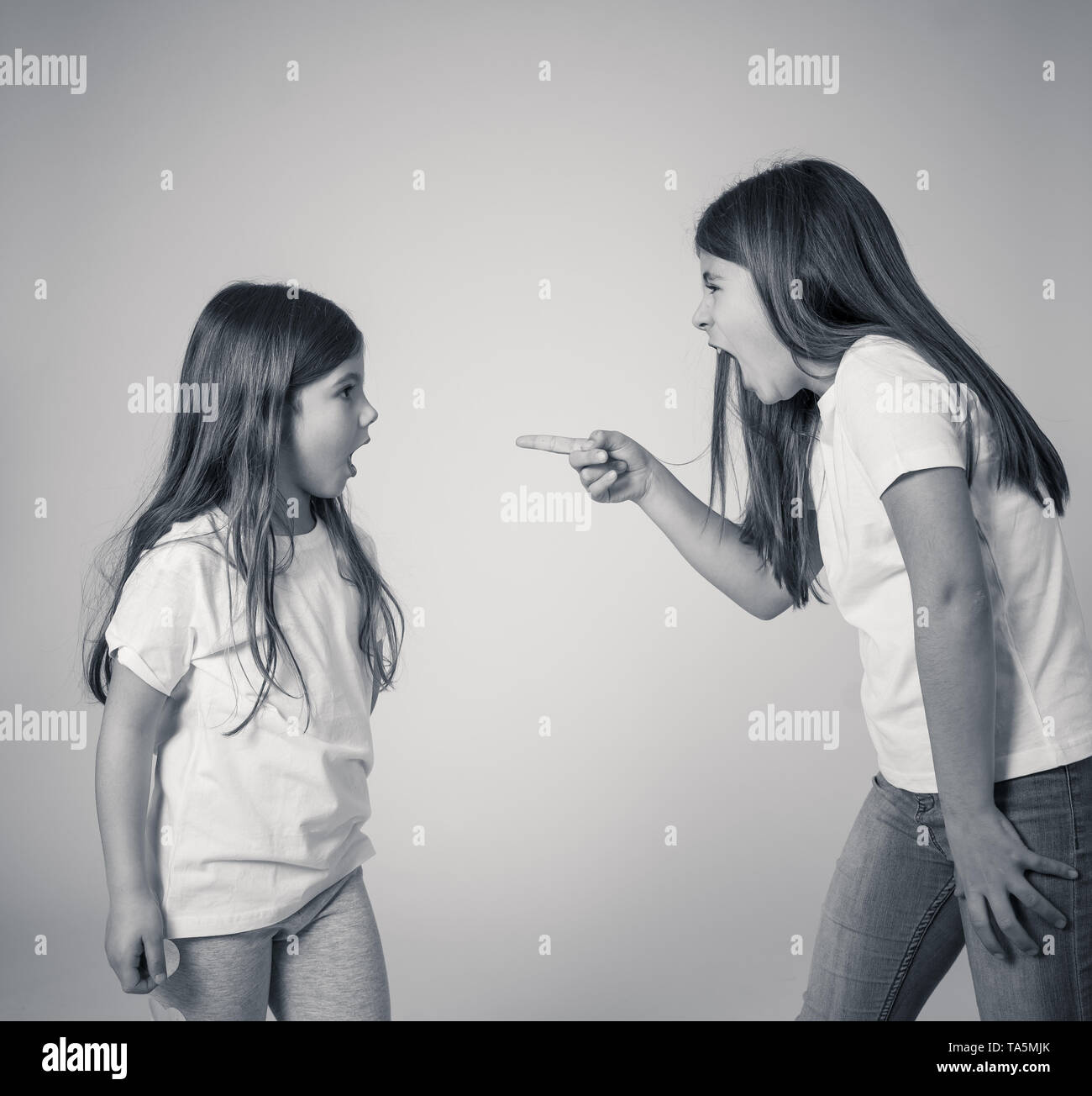 Portrait of siblings interacting having an argument. Older sister shouting and making furious gestures to her angry sad younger sister. Siblings bad r Stock Photo