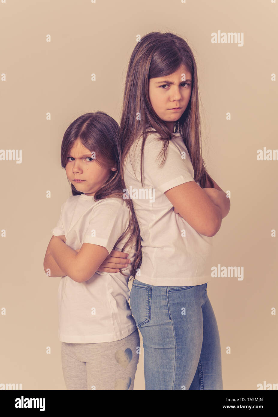 Portrait of two young siblings standing back to back not talking to each other after having an argument. Sisters not interacting angry and mad one to  Stock Photo