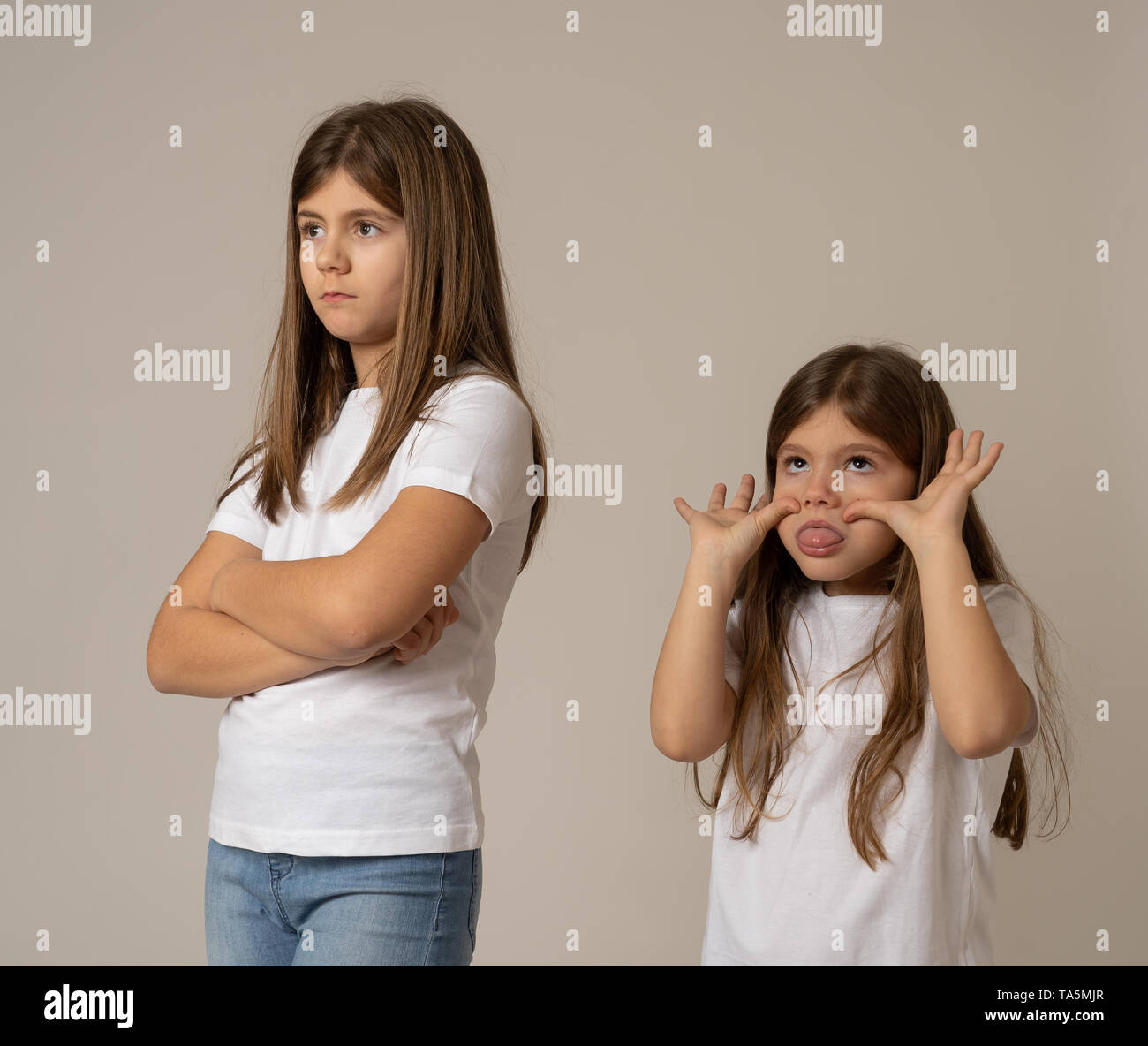 Portrait of siblings interacting having an argument. young sister sticking tongue out and making funny faces to her angry sad older sister not talking Stock Photo