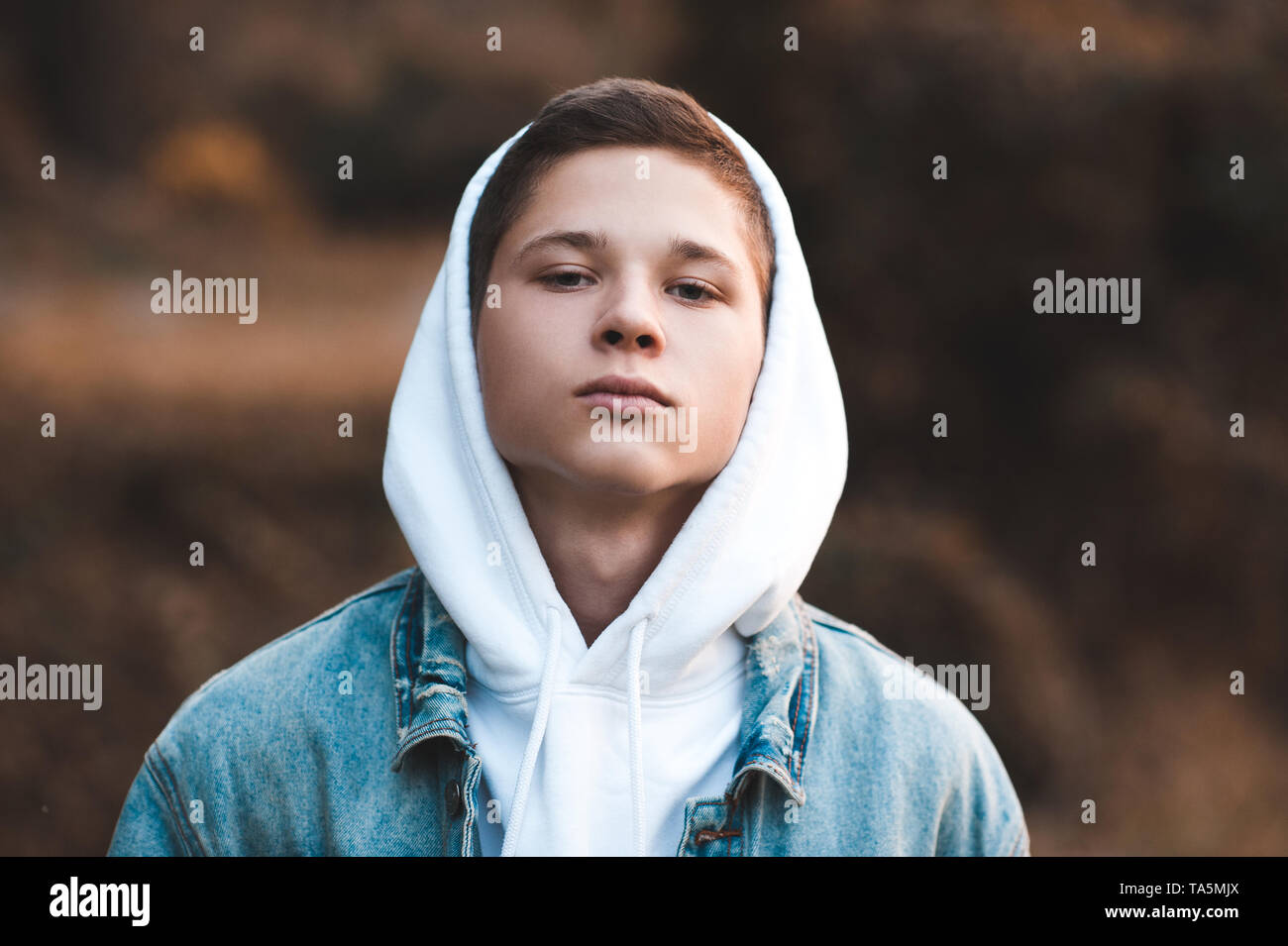 Teen boy 16-17 year old wearing white hoodie and denim jacket closeup. Looking at camera. 20s. Stock Photo