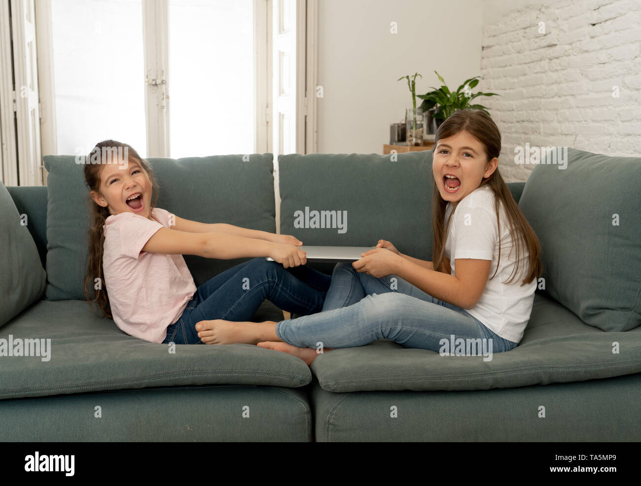Younger and older girls fighting for laptop arguing over playing on the internet. Lifestyle portrait of sisters not sharing computer in Relationship b Stock Photo