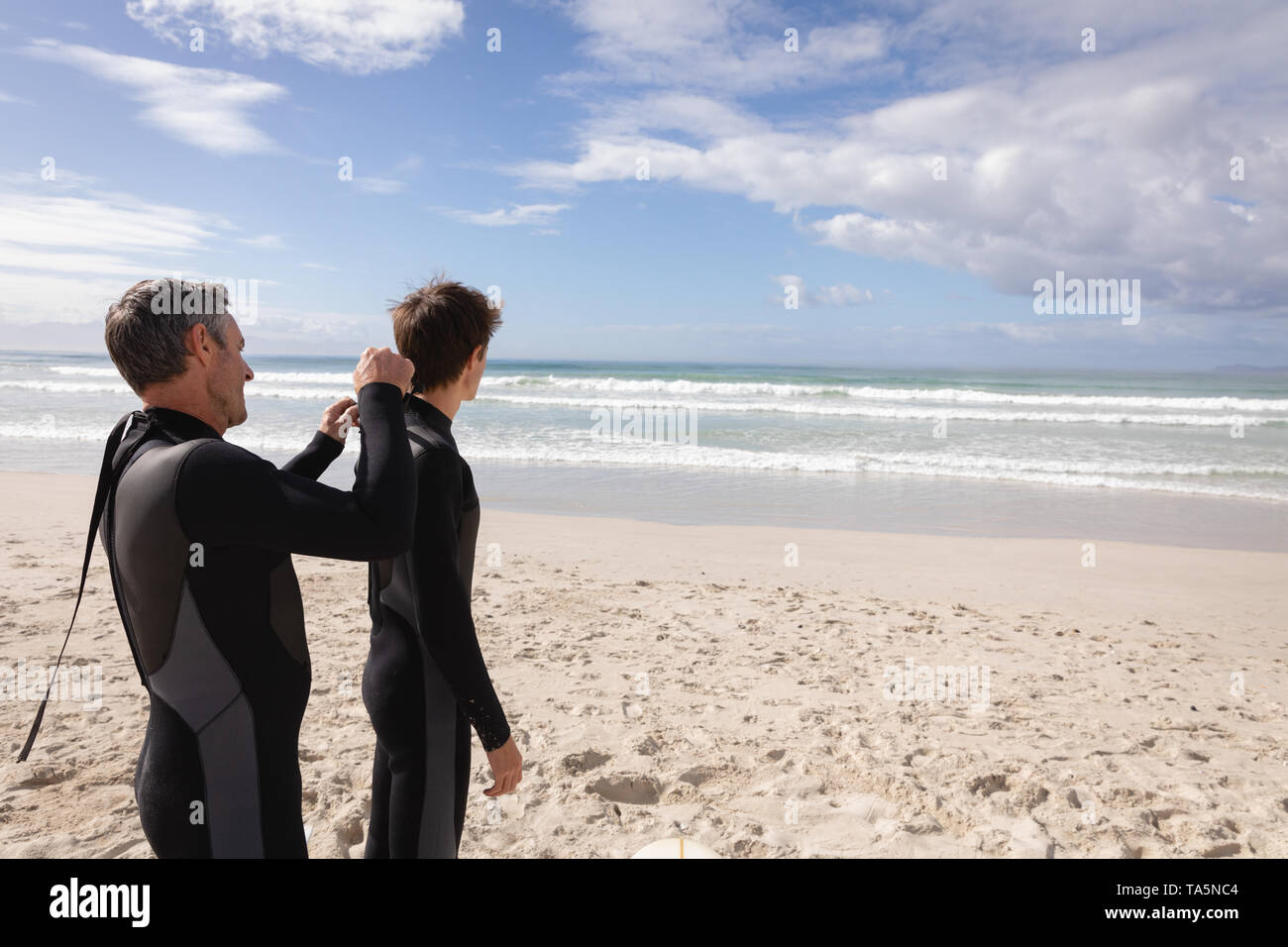 Father assist son to wear wetsuit at beach Stock Photo