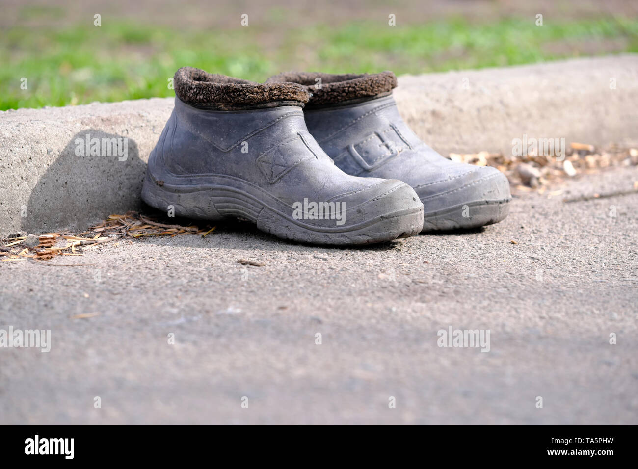 Two old rubber boots stand on the sidewalk near the curb on a bright spring day Stock Photo