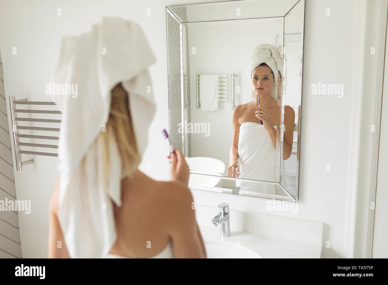 Beautiful woman standing in front of mirror while holding toothbrush Stock Photo