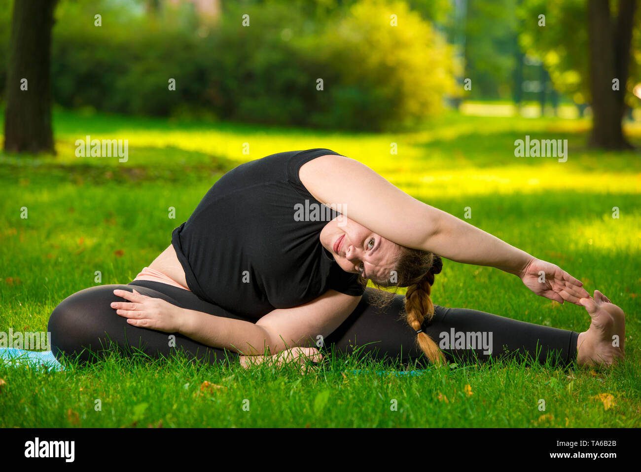 flexible plus size woman doing yoga in the park on the lawn Stock Photo