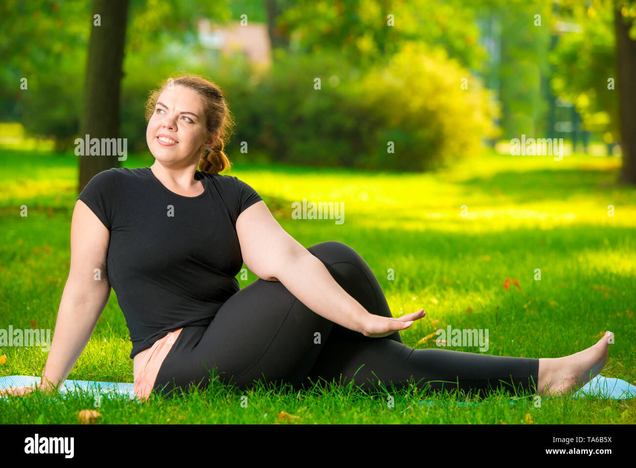 happy over sized woman in the park doing yoga early in the morning on the lawn Stock Photo