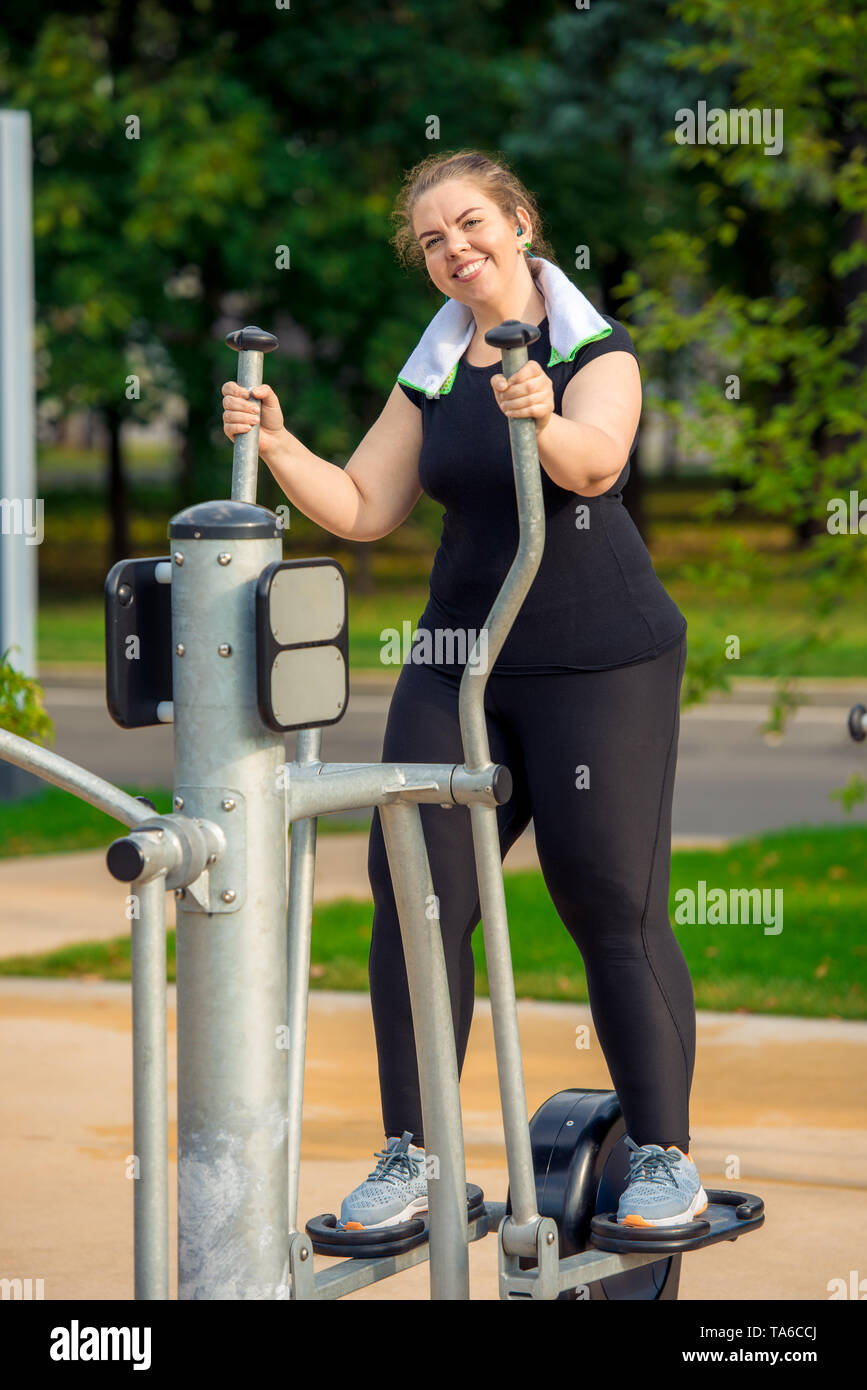 active fat woman without complexes is engaged on the stepper simulator in the park Stock Photo