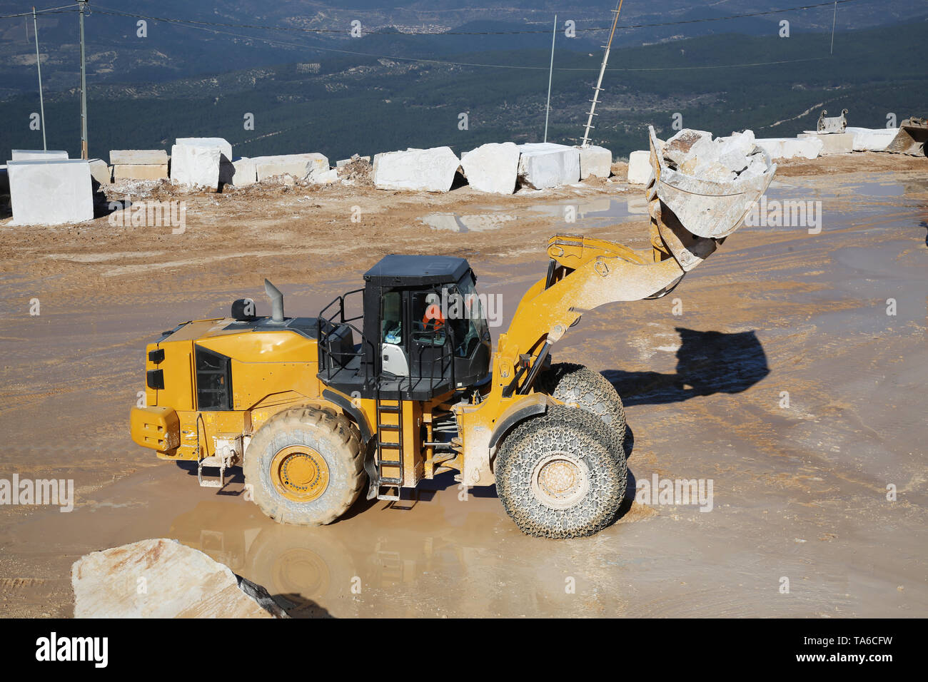 A big loader machine working on marble quarry. A loader loading marble block. Heavy machinery working on mining quarry. Stock Photo
