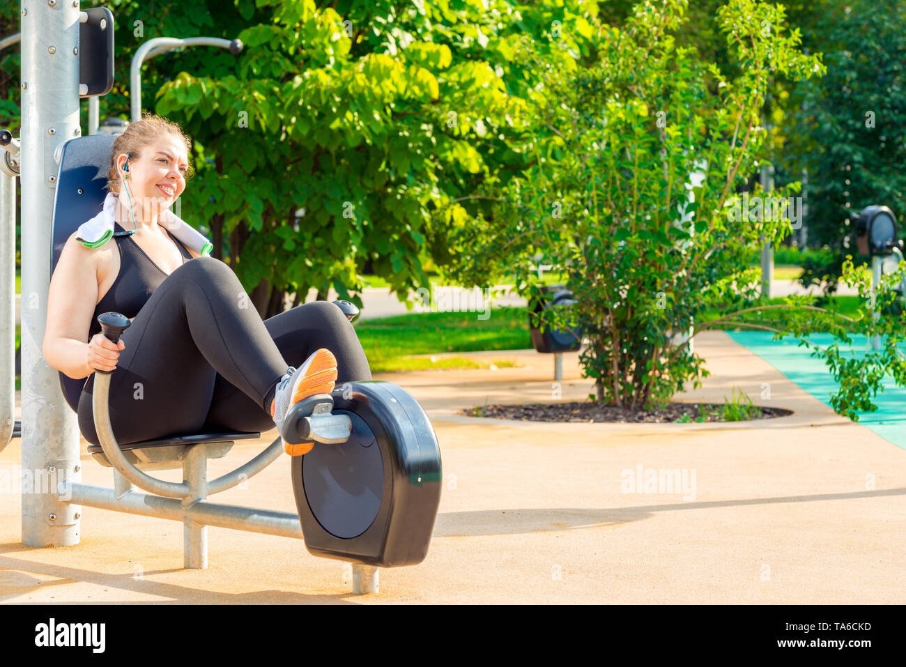 active oversized woman doing exercise on a stationary bike in a city park Stock Photo