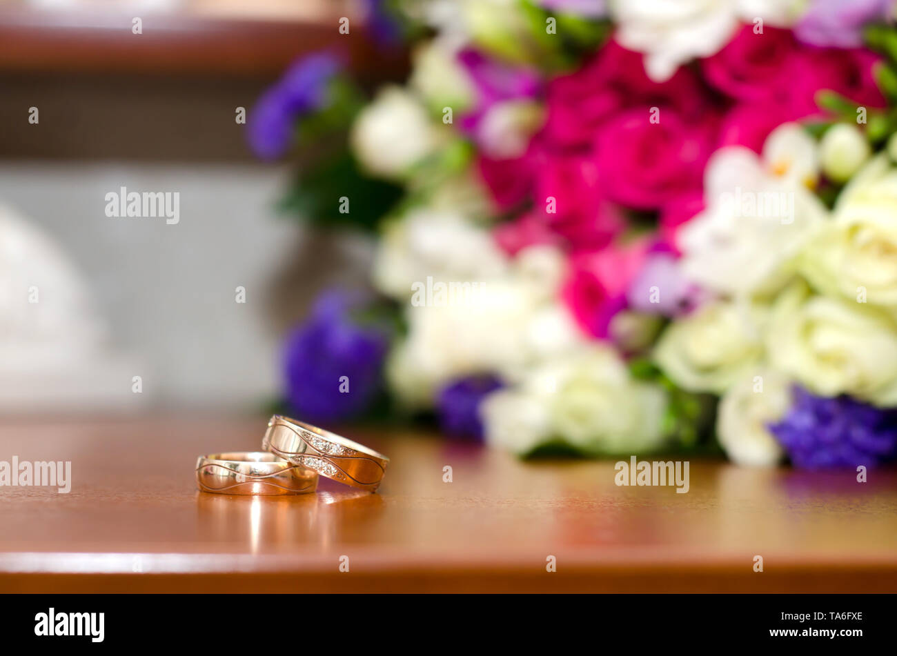 Bright picture with wedding rings and colorful wedding bouquet on the table Stock Photo