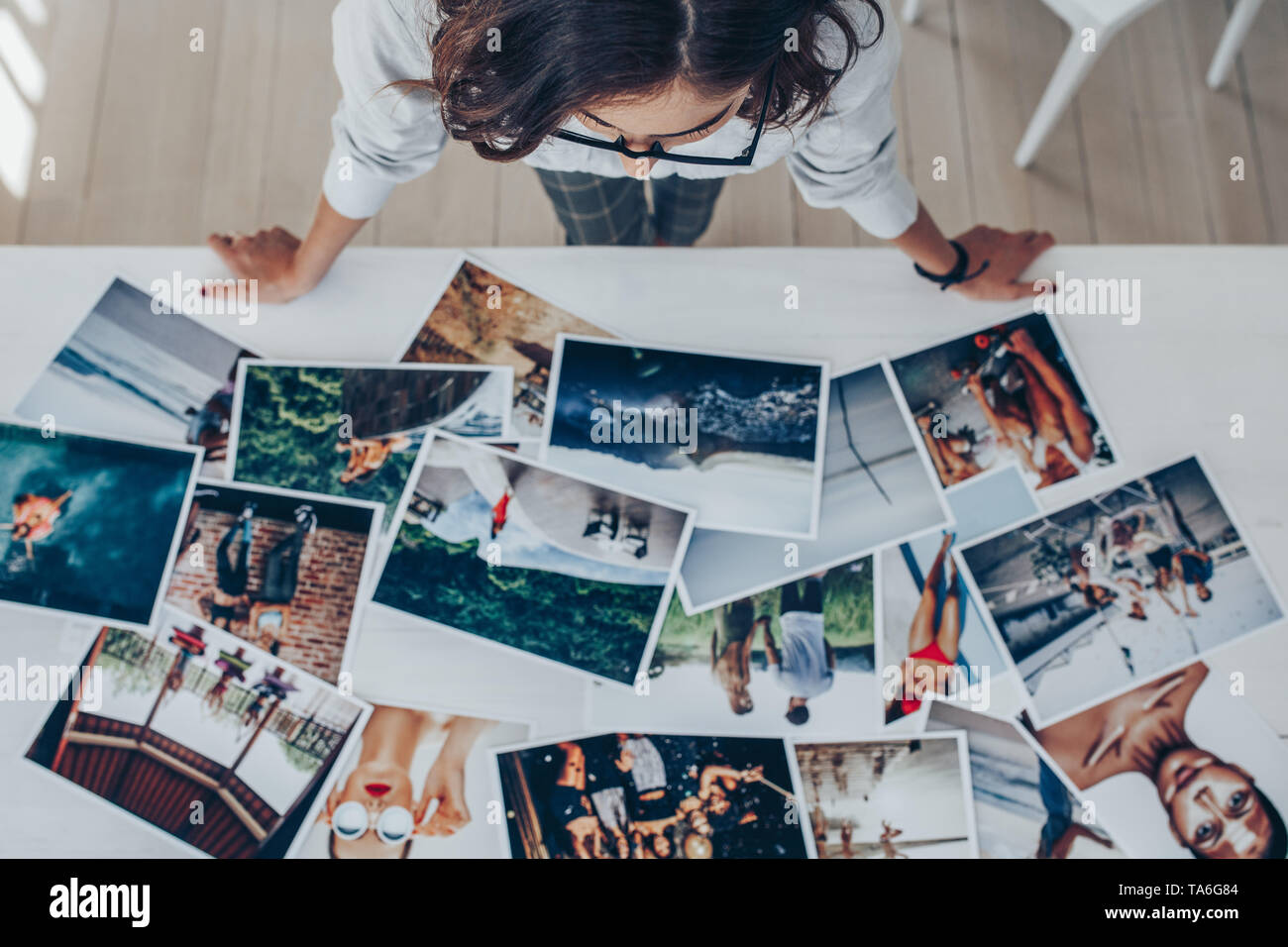 Top view of a female photographer working in studio looking at the prints lying on desk. Female photographer choosing the best image from several phot Stock Photo