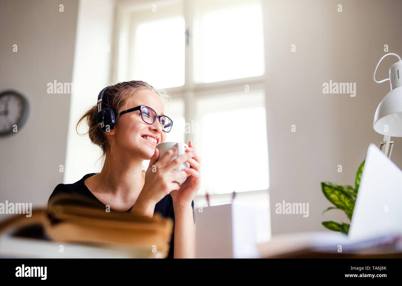 A young female student sitting at the table, using headphones when ...