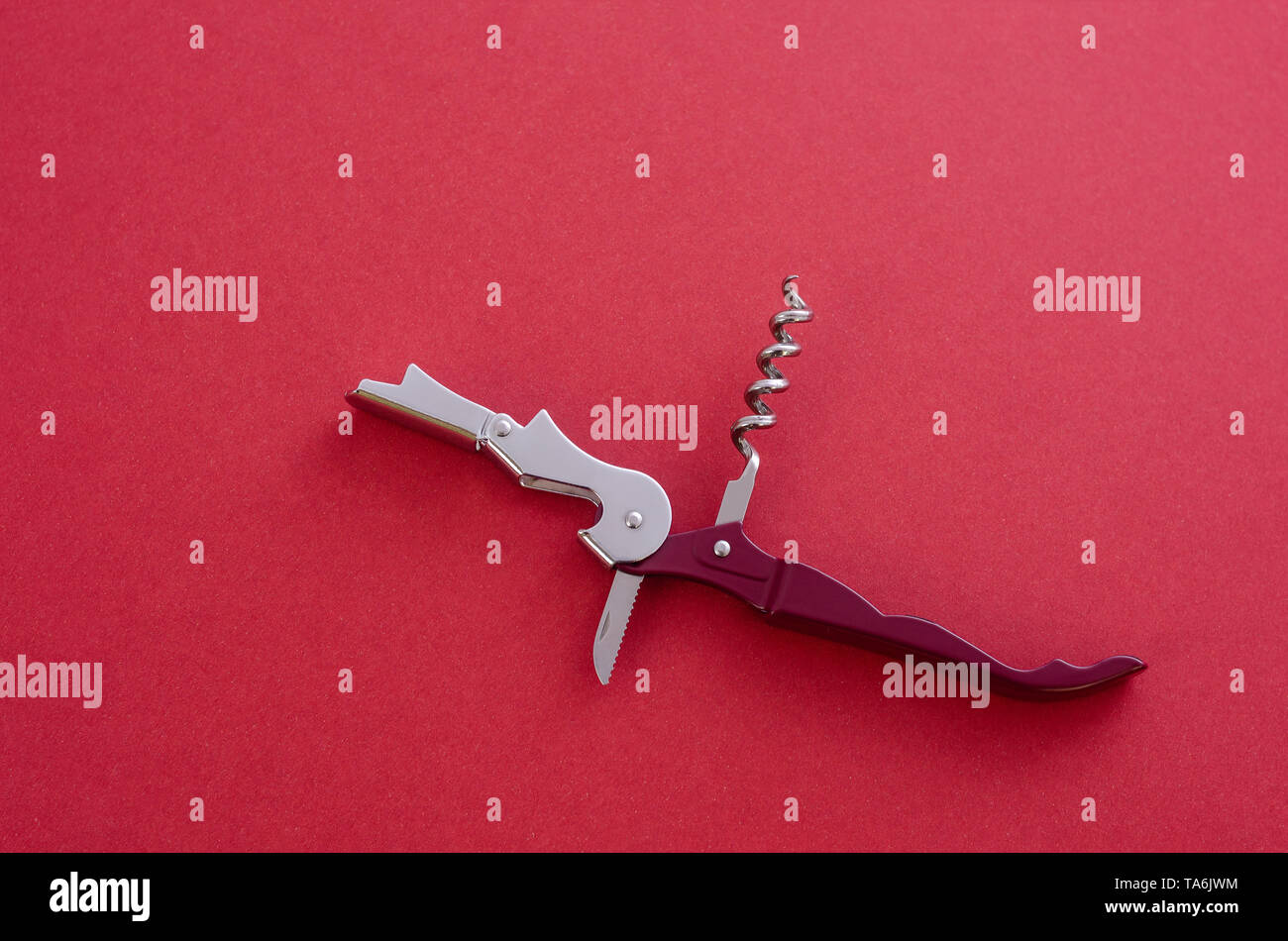 Opened sommelier's knife with corkscrew and bottle opener, waiter's knife professional, on red background. Stock Photo
