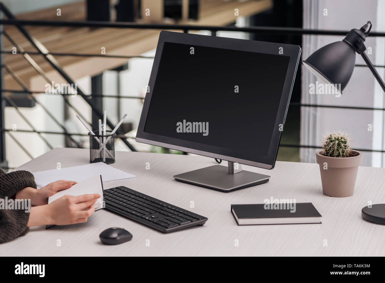 partial view of woman holding notebook near computer at workplace with ...