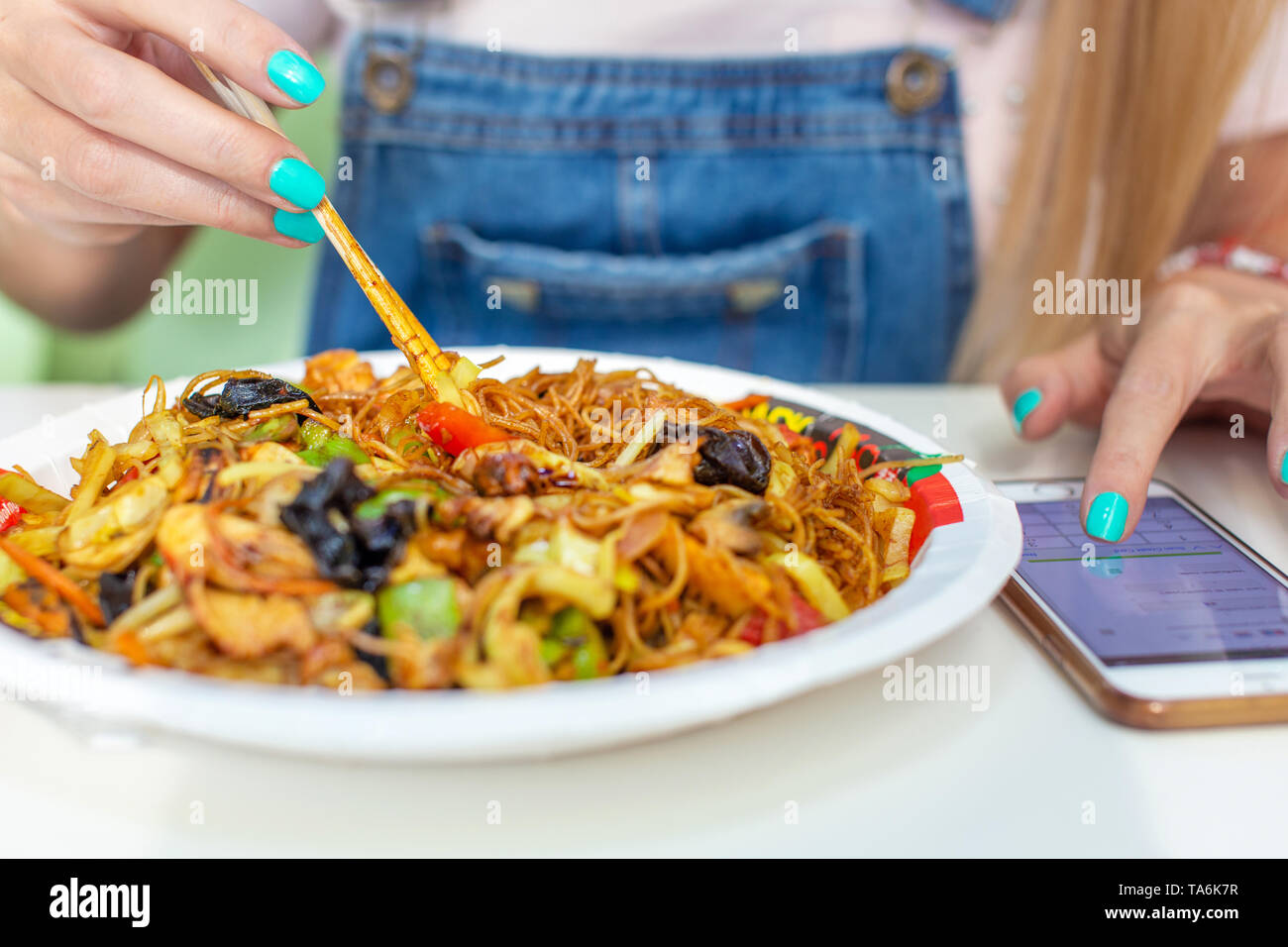 Woman eating chinese noodle with chicken and messaging on smartphone Stock Photo