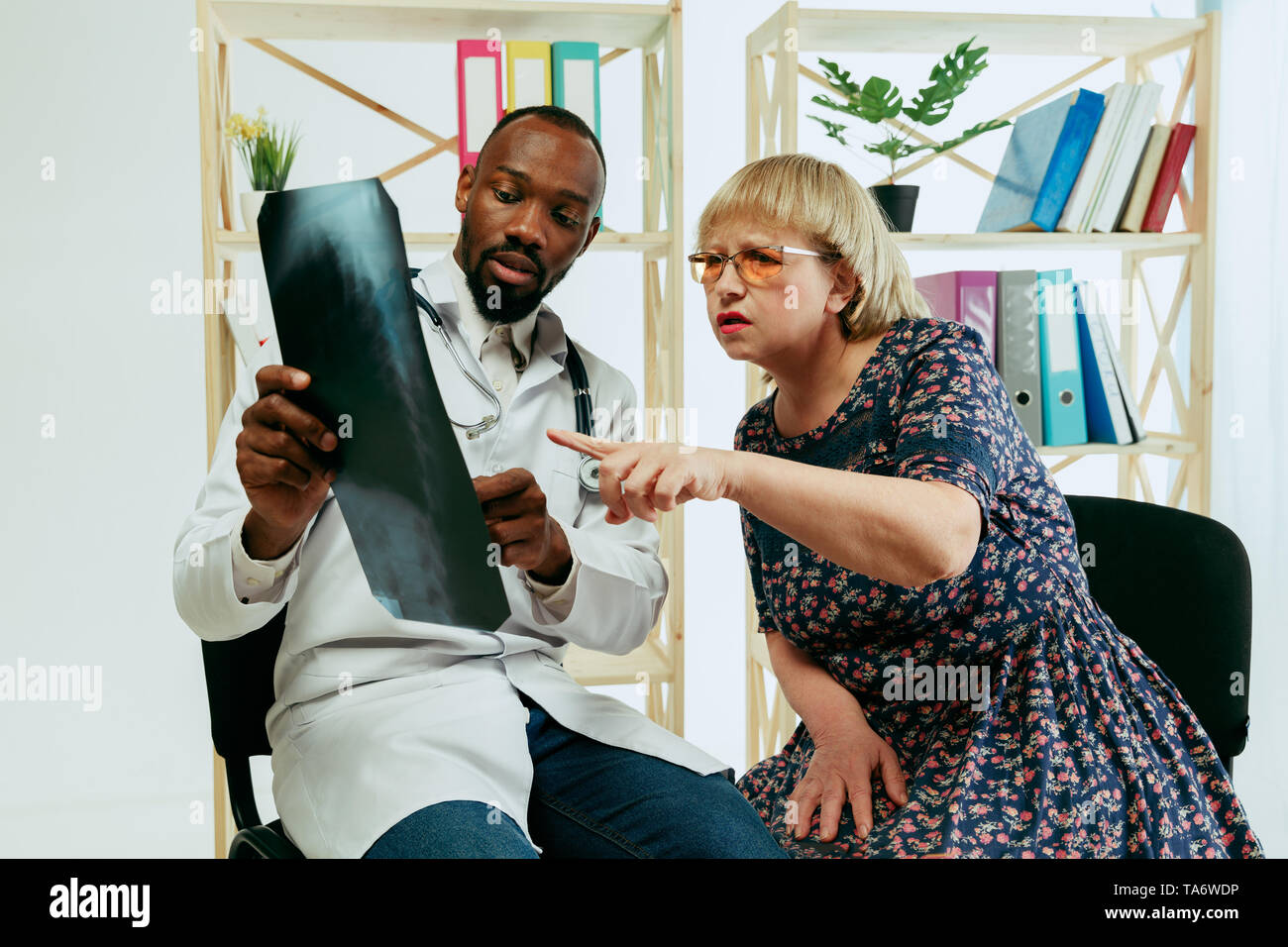 A senior woman visiting a therapist at the clinic for getting consultation and checking her health. Talking to a doctor. Lifestyle portrait at the cab Stock Photo