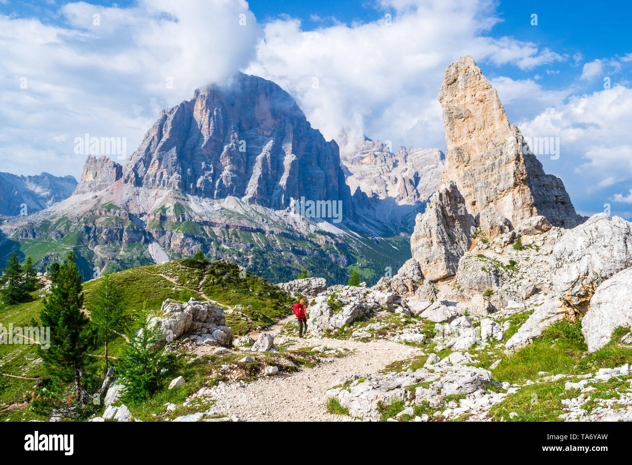 Girl with red backpack on Cinque Torri tour, with views towards Castelletto, Tofana di Rozes, Tofana di Mezzo in the background. Hiking holiday in the Stock Photo