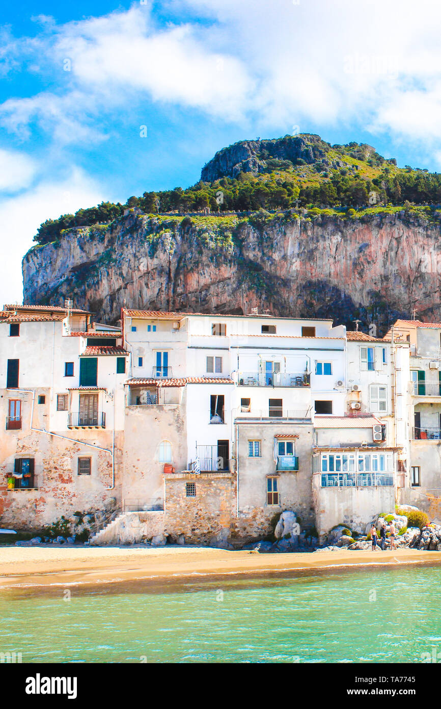Beautiful traditional houses on the coast of Tyrrhenian sea in Cefalu, Sicily, Italy. Behind the buildings magnificent rock overlooking the bay. The amazing Sicilian city is a popular tourist spot. Stock Photo