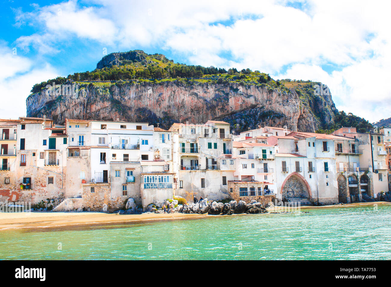 Amazing old houses on the coast of Tyrrhenian sea in beautiful Cefalu, Sicily, Italy. Behind the buildings marvelous rock overlooking the coast. The Sicilian city is a popular tourist attraction. Stock Photo