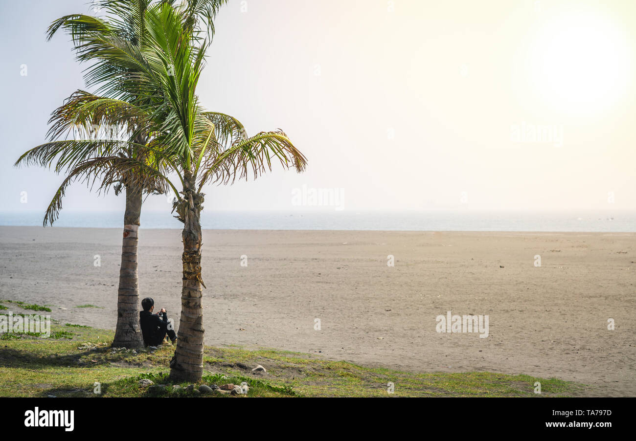 Asian man silhouette looking at sunset under a palm tree on the beach of Cijin island Kaohsiung Taiwan Stock Photo