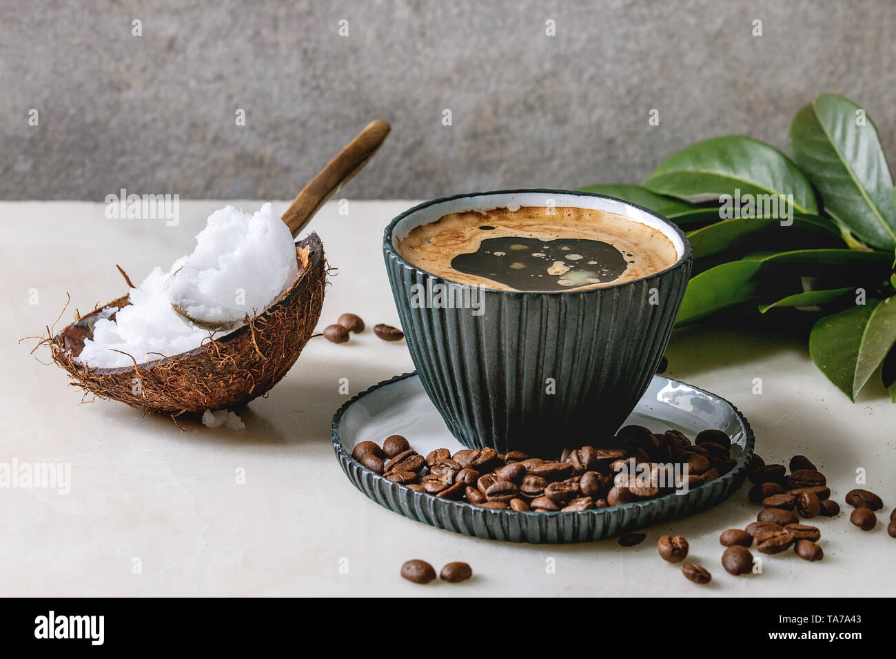 Bulletproof coffee. Keto diet coffee in blue ceramic cup with organic coconut cold press oil in spoons with beans and green branch on white marble tab Stock Photo