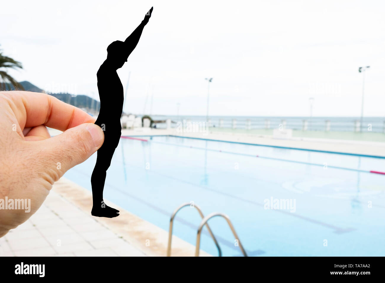 closeup of the hand of a man with a black paper cutout in the shape of a man about to throw himself into a swimming pool Stock Photo