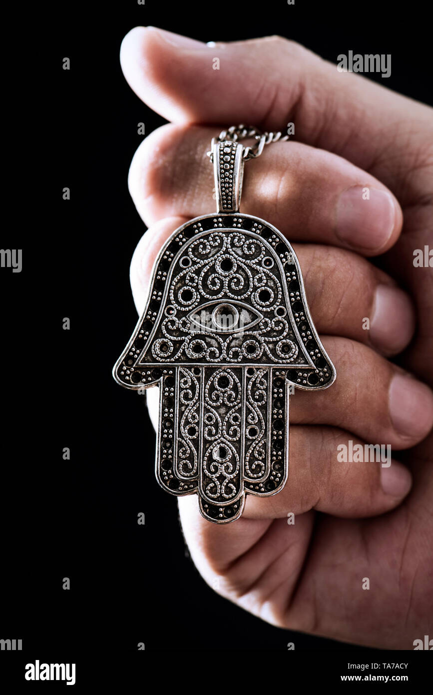 closeup the hand of a young man holding an old hamsa amulet, also known ...