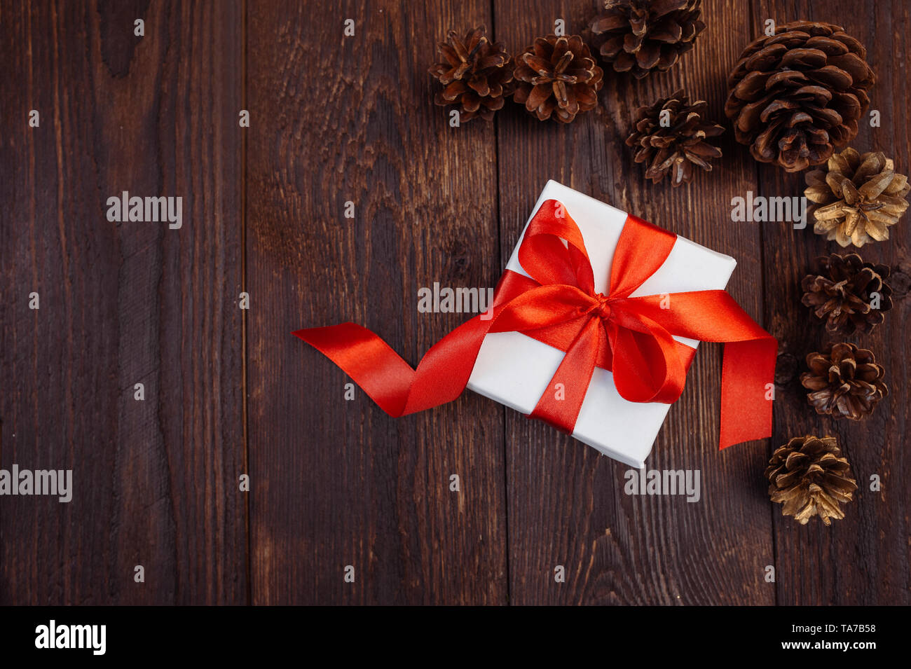 Christmas greetings card. White gift box with red ribbon and bumps on a wooden background with place for your text Stock Photo