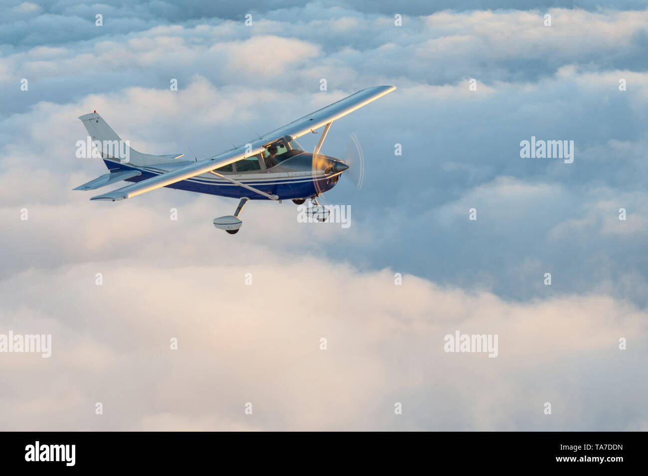 Stunning view of a blue and white little private Cessna airplane browsing the sky over fluffy clouds. Stock Photo