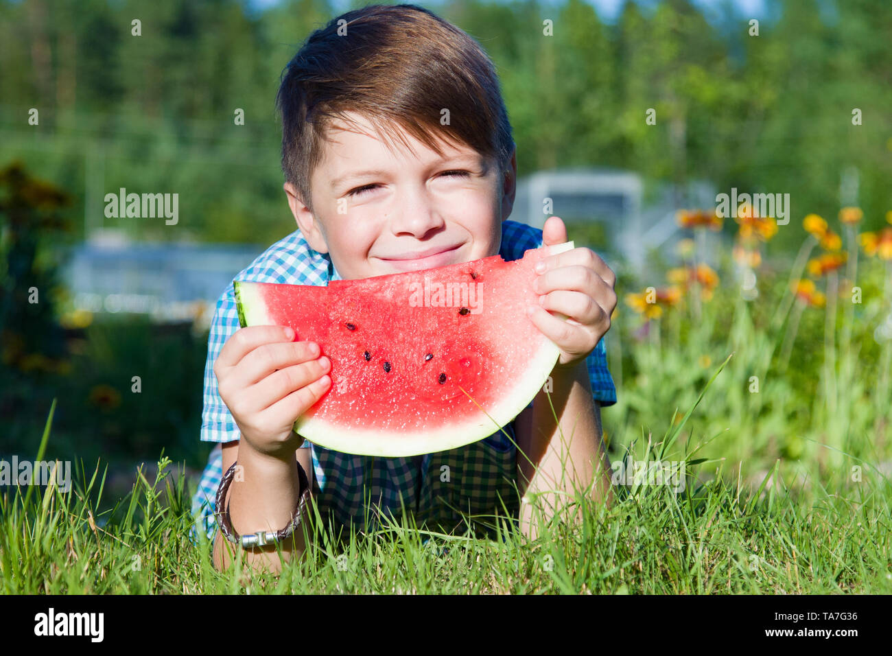 Funny boy eats watermelon outdoors in summer park, healthy food Stock Photo