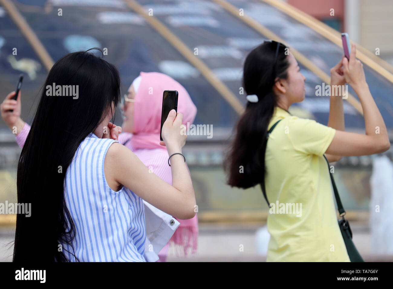 Happy asian and muslim girls make a selfie with smartphones on Manege square, selective focus. People using mobile phones, young women taking pictures Stock Photo
