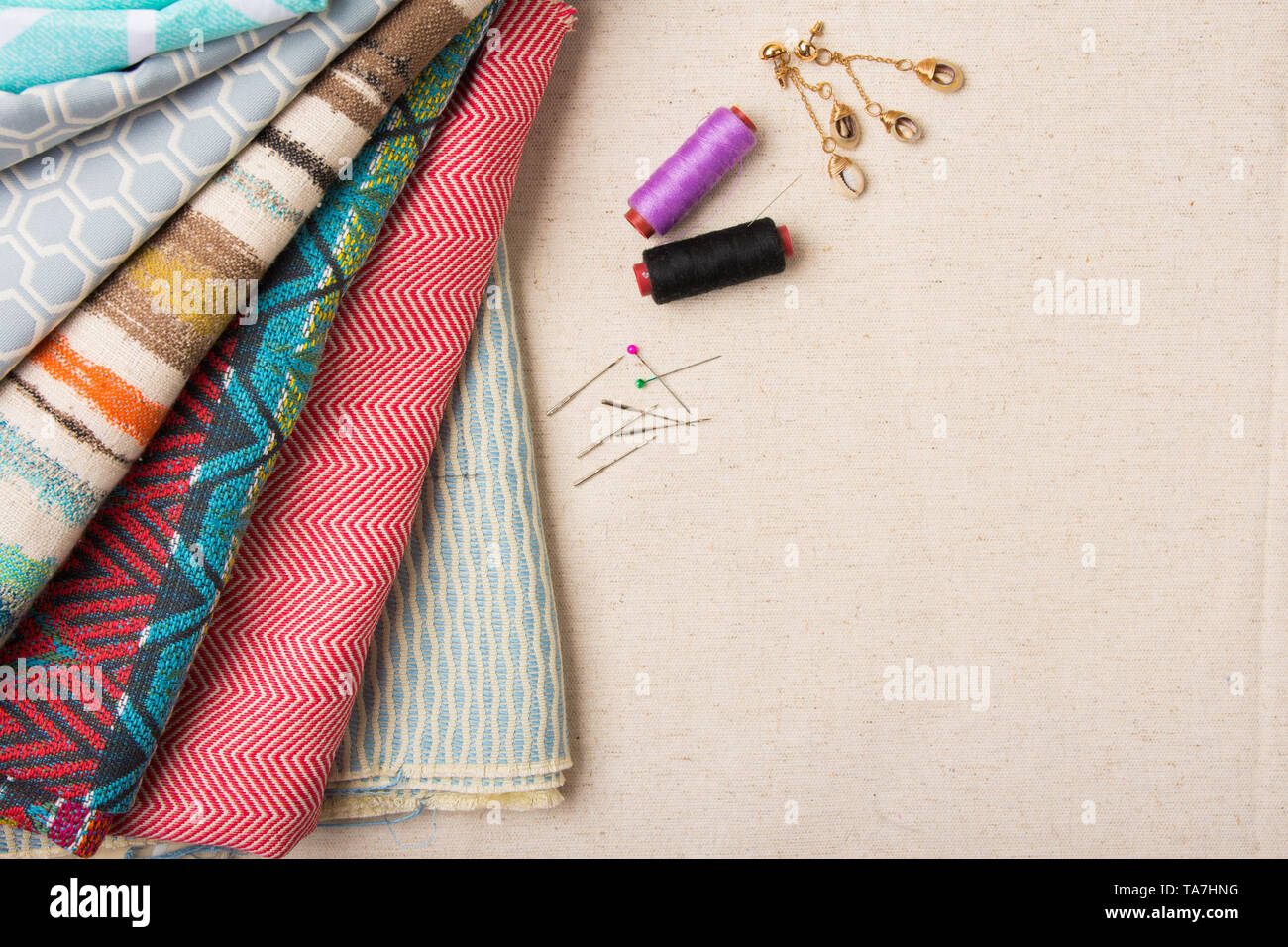 A variety of colourful fabric with assorted sewing pins and thread flat ...